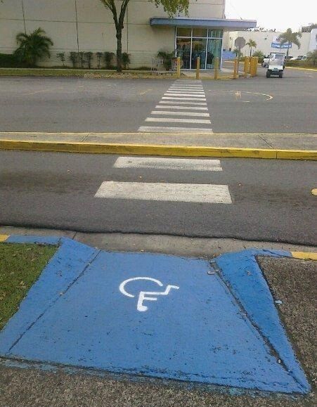 Senda peatonal con rampa para personas con discapacidad que tiene una vereda en el centro que no permite el cruce completo.